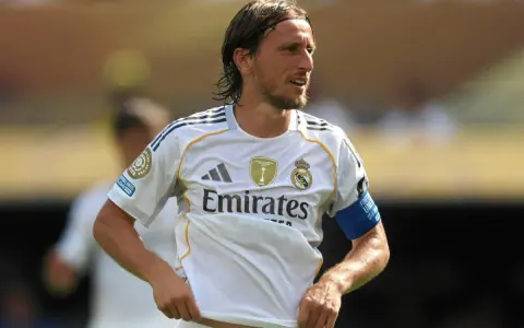 Luka Modrić w białej koszulce Realu Madryt, gdzie gra, z opaską na ramieniu.