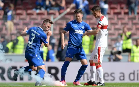 Piłkarze Karlsruher SC w niebieskich strojach, jeden z nich z numerem 3, otoczeni dymem z rac.