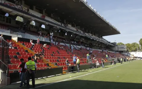 Puste trybuny stadionu Vallecas, z kilkoma osobami siedzącymi i stojącymi.