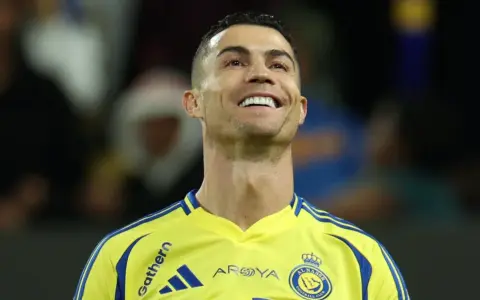 Uśmiechnięty Cristiano Ronaldo w żółtej koszulce Al Nassr. To właśnie w tym klubie gra Ronaldo.