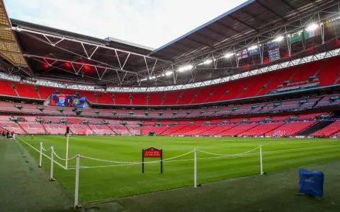Pusta, czerwona trybuna stadionu Wembley, największego stadionu na świecie, z zieloną murawą i tabliczką "Prosimy nie wchodzić na trawę".