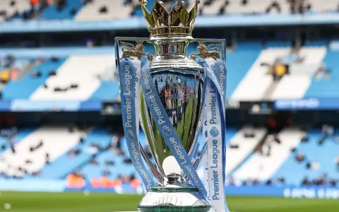 Trofeum za mistrzostwo Anglii, błyszczące i ozdobione wstążkami Premier League, stoi na tle stadionu.