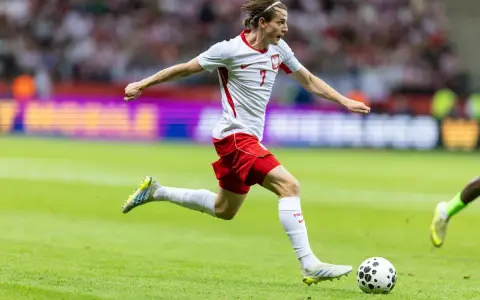 Jakub Kamiński w akcji, biegnie z piłką na boisku. Jego obecne drużyny to reprezentacja Polski i VfL Wolfsburg.