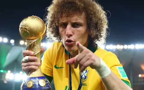 Piłkarz z Brazylii, z bujną fryzurą, triumfalnie trzyma złoty puchar Konfederacji FIFA.