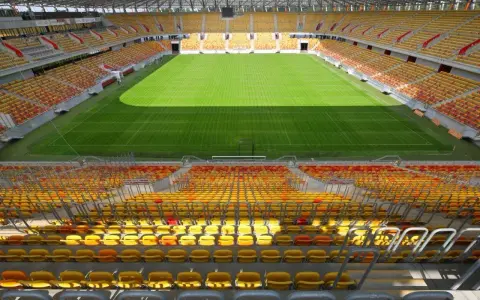 Pusta trybuna stadionu Jagiellonii, z żółtymi i czerwonymi siedzeniami. Pojemność obiektu robi wrażenie.