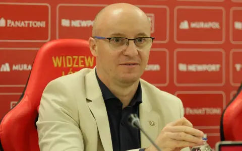 Nowy trener Widzewa w jasnej marynarce, siedzi na czerwonym fotelu z logo klubu.
