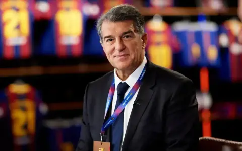 Uśmiechnięty prezes Barcelony, Joan Laporta, w garniturze, z identyfikatorem FC Barcelona na szyi.