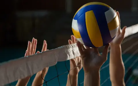 Piłka do siatkówki tuż nad siatką, ręce graczy gotowe do akcji. Zastanawiasz się, ile trwa mecz siatkówki? To zależy od dynamiki gry!