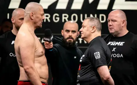 Dwóch zawodników na ważeniu przed walkami Fame MMA, z mikrofonem i ochroniarzami.