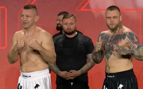 Dwóch zawodników MMA, jeden z tatuażami na klatce piersiowej, gotowych do walki. W tle stoi mężczyzna.