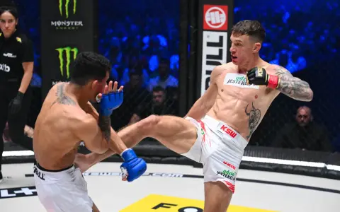 Zacięta walka na KSW 115 karta walk. Zawodnik w białych spodenkach wykonuje wysokie kopnięcie, przeciwnik blokuje je rękawicą.