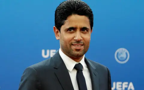 Nasser Al-Khelaifi w garniturze na tle niebieskiej ściany z logo UEFA.