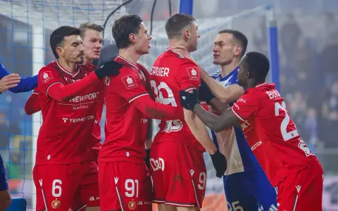 Piłkarze w czerwonych strojach kłócą się z zawodnikiem w niebieskiej koszulce.
