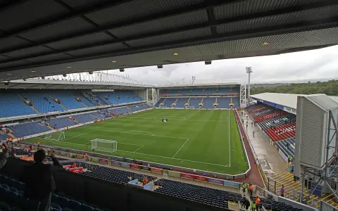 Widok na murawę i trybuny stadionu Ewood Park. Puste miejsca na niebieskich i czerwonych siedzeniach.