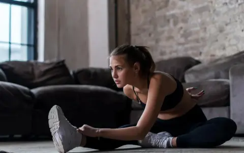 Młoda kobieta w sportowym stroju wykonuje ćwiczenia rozciągające na podłodze. Widać, co daje rozciąganie po treningu: poprawia elastyczność i relaksuje.