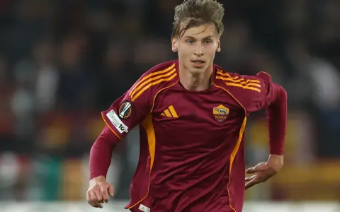 Piłkarz AS Roma w bordowej koszulce z żółtymi pasami, gotowy do gry przeciwko Genoa CFC.