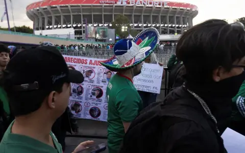 Tłum ludzi przed stadionem Azteca. Na pierwszym planie mężczyzna w meksykańskim kapeluszu, obok baner z portretami zaginionych.