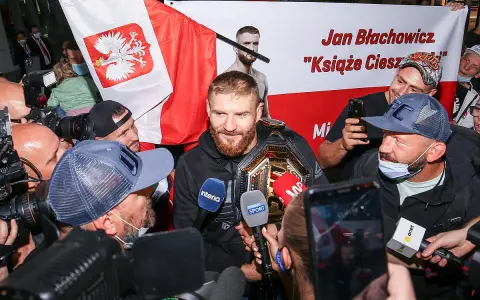 Jan Błachowicz, "Książę Cieszyński", mistrz UFC, otoczony przez fanów i dziennikarzy z polską flagą. Polacy w UFC świętują sukces.