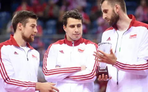 Trzech siatkarzy w strojach z biało-czerwoną flagą Polski. Jeden z nich trzyma puchar, symbolizujący, kto jest aktualnym mistrzem świata w siatkówce.