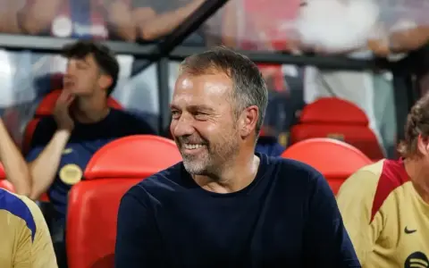 Uśmiechnięty trener Barcelony, siedzący na ławce rezerwowych, w otoczeniu innych członków sztabu.