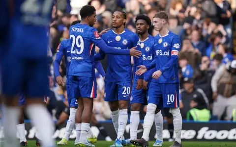 Piłkarze Chelsea w niebieskich strojach rozmawiają na boisku. Widać numery 29, 20 i 10.
