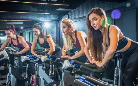 Cztery kobiety ćwiczą na rowerach stacjonarnych. Ile powinien trwać trening cardio? To zależy od celów, ale często 30-60 minut to dobry punkt wyjścia.