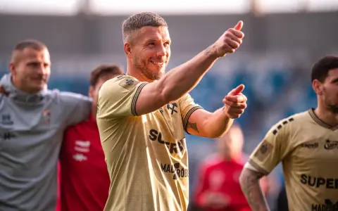 Uśmiechnięty Lukas Podolski pokazuje kciuk w górę, jakby podsumowywał swoje świetne statystyki.