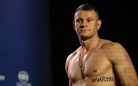 KSW relacja: Muskularny zawodnik MMA z tatuażem na klatce piersiowej pozuje przed kamerą.