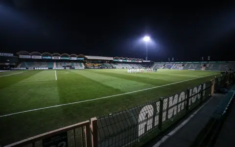 Piłkarze na murawie stadionu Górnik Łęczna, oświetlonego jupiterami.