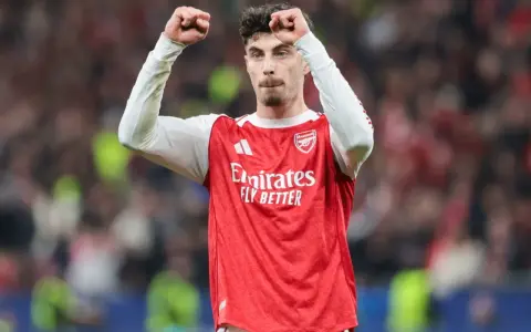 Piłkarz Arsenalu świętuje klasyczny hattrick, wznosząc pięści w geście triumfu na tle trybun.