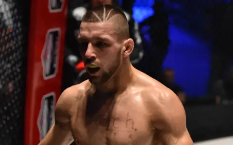 Zacięty zawodnik MMA z charakterystyczną fryzurą i ochraniaczem na zęby, gotowy do walki.