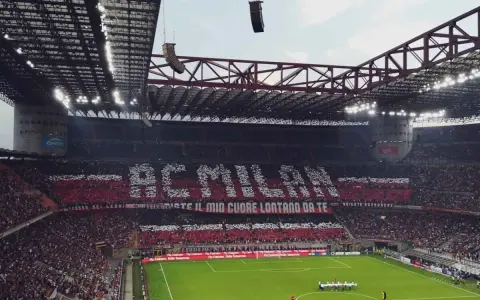 Trybuna stadionu San Siro w Mediolanie wypełniona kibicami AC Milan, tworzącymi napis "AC MILAN" i transparent "FOSSI DEI LEONI, VECCHIESTE IL MIO CUORE LONTANO DA TE".