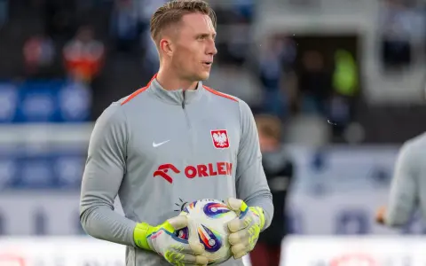 Bramkarz w szarej bluzie z orłem i napisem ORLEN, trzymający piłkę. Kolejny z polscy piłkarze za granicą, gotowy do gry.