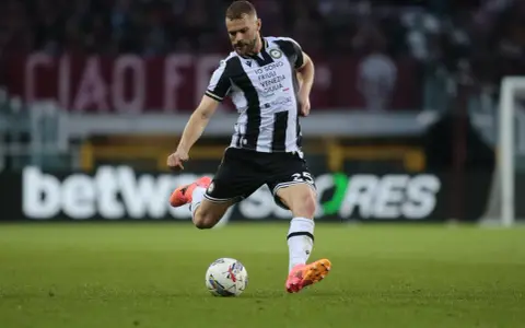 Piłkarz Jesper Karlström w czarno-białej koszulce Udinese Calcio kopie piłkę na zielonej murawie stadionu.