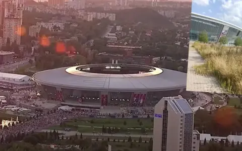 Donbass Arena w blasku zachodzącego słońca, otoczona miejskim krajobrazem i tłumami ludzi.