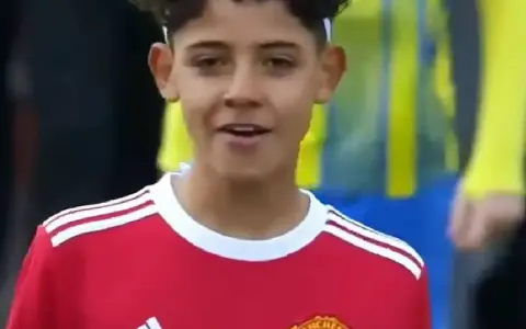 Młody piłkarz w czerwonej koszulce Manchester United, przypominający syna Cristiano Ronaldo. Jego wiek sugeruje, że to początki kariery.