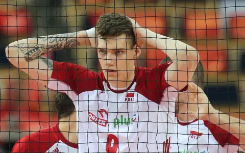 Młody siatkarz reprezentacji Polski z tatuażami na ramieniu, z rękami na głowie, w białej koszulce z czerwonymi elementami.
