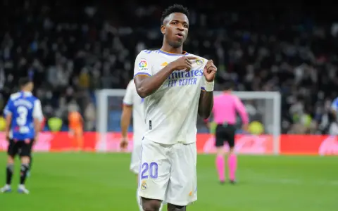 Vinicius Jr. w białej koszulce Realu Madryt z numerem 20, świętuje bramkę na tle trybun.