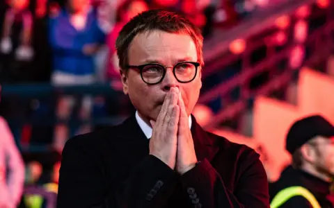 Właściciel Wisły Kraków, w okularach, z rękami złożonymi do modlitwy, wpatruje się w dal.
