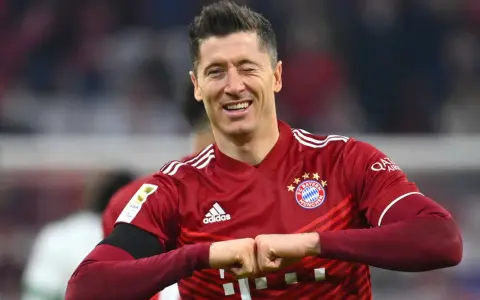 Piłkarz Robert Lewandowski w czerwonej koszulce Bayernu Monachium, uśmiecha się i zaciska pięści.