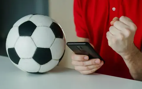 Piłka nożna i smartfon. Kibic sprawdza wynik, licząc na powyżej 2.5 gola.
