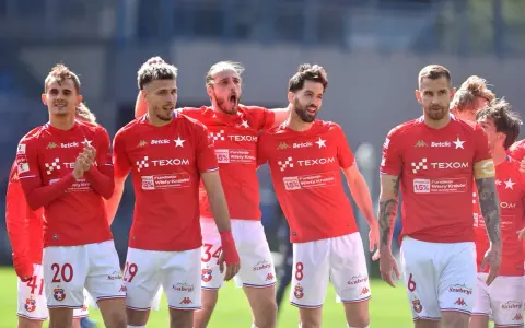 Piłkarze Wisły Kraków w czerwonych strojach, z numerami na koszulkach i spodenkach, świętują. W tle trybuny. #wisla #krakow #transfery
