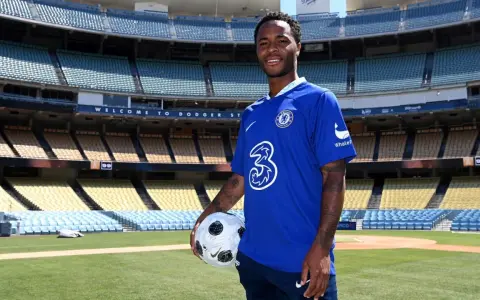 Raheem Sterling w niebieskiej koszulce Chelsea z piłką, na tle stadionu. Jego statystyki w klubie są obiecujące.