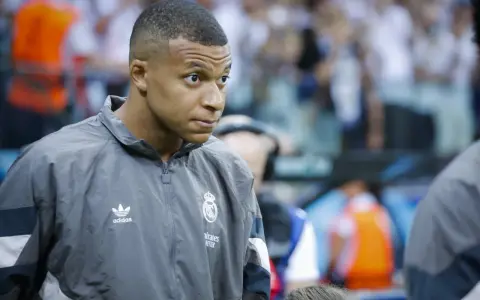 Kylian Mbappé w szarej kurtce z logo Realu Madryt, gotowy do gry.