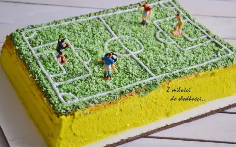 Jak zrobić tort boisko do piłki nożnej? Zielona posypka imituje trawę, a białe linie wyznaczają pole gry. Figurki piłkarzy i piłka dodają realizmu.