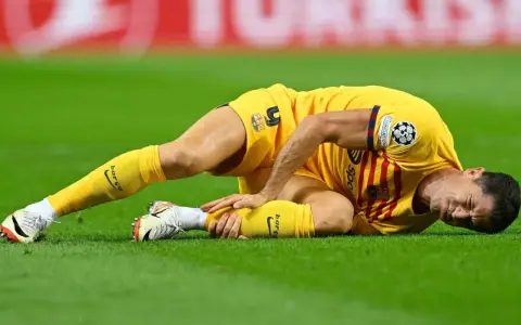 Piłkarz w żółtej koszulce leży na trawie, trzymając się za nogę. Wygląda na to, że Robert Lewandowski kontuzja uniemożliwiła mu dalszą grę.
