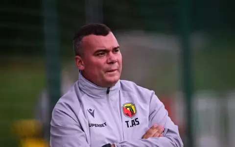 Trener Jagiellonii, z rękami skrzyżowanymi na piersi, w szarej kurtce z herbem klubu.