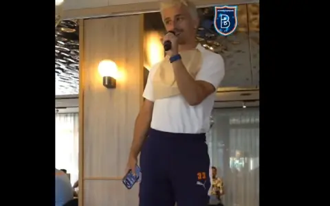 Młody mężczyzna z blond włosami, w koszulce i granatowych spodenkach z numerem 33, trzyma mikrofon. W tle logo İstanbul Başakşehir.