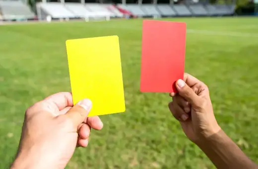 Dwie ręce trzymają żółtą i czerwoną kartkę na tle boiska piłkarskiego. Sędzia pokazuje czerwoną kartkę w piłce nożnej.