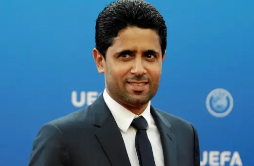 Nasser Al-Khelaifi w garniturze na tle niebieskiej ściany z logo UEFA.